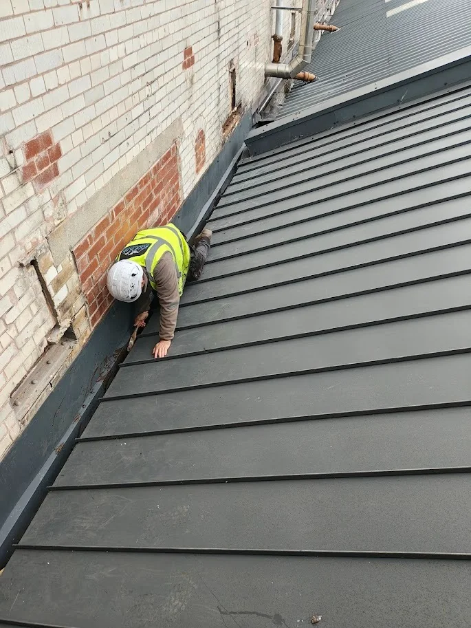 Roofer inspecting flashing on a standing seam metal roof